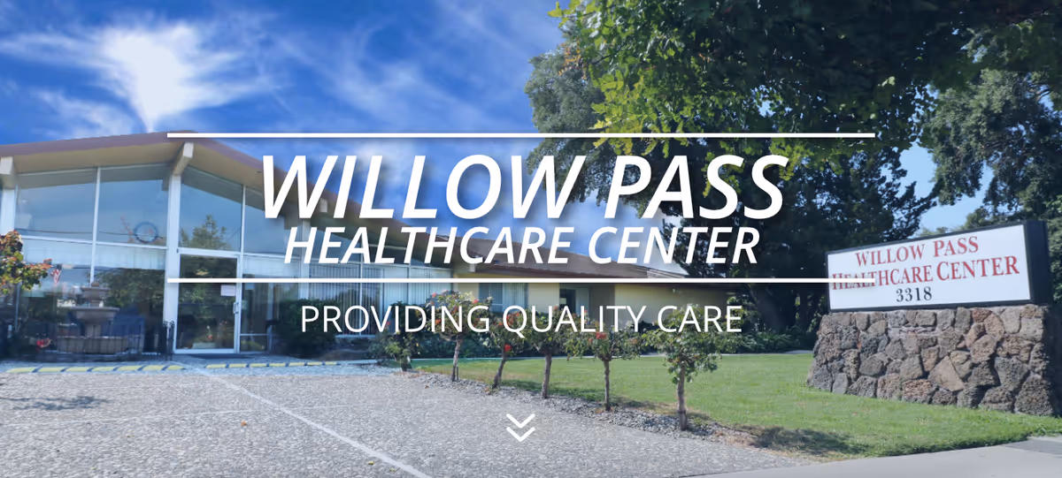 Exterior view of Willow Pass Healthcare Center building with a clear blue sky, a driveway, green lawn, small trees, and a stone sign displaying the facility name and address.