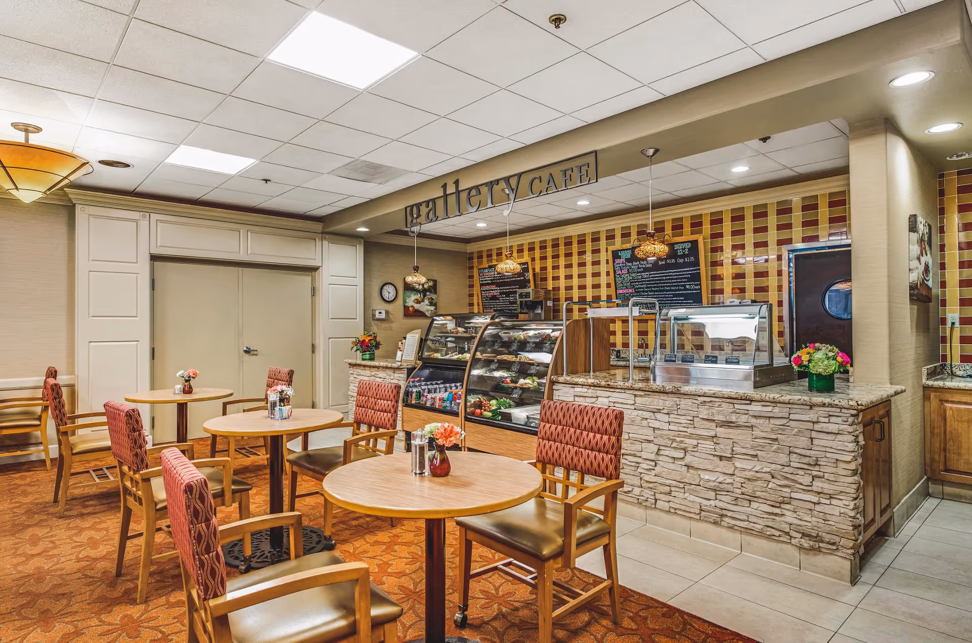 Cozy café-style dining area with round tables, upholstered chairs, and a service counter beneath a 'gallery CAFE' sign.