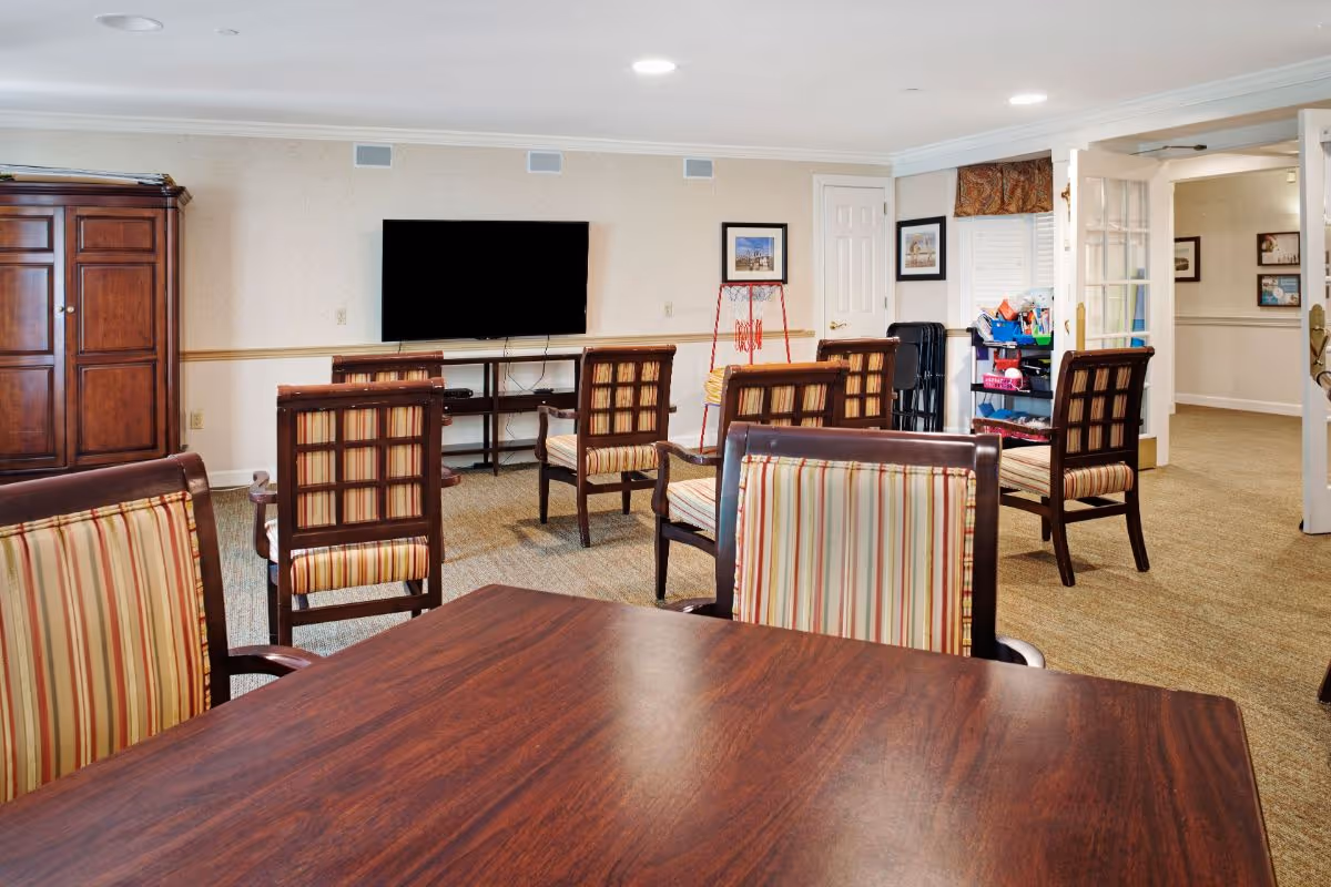 Community lounge with a wooden table and striped chairs facing a wall-mounted TV.
