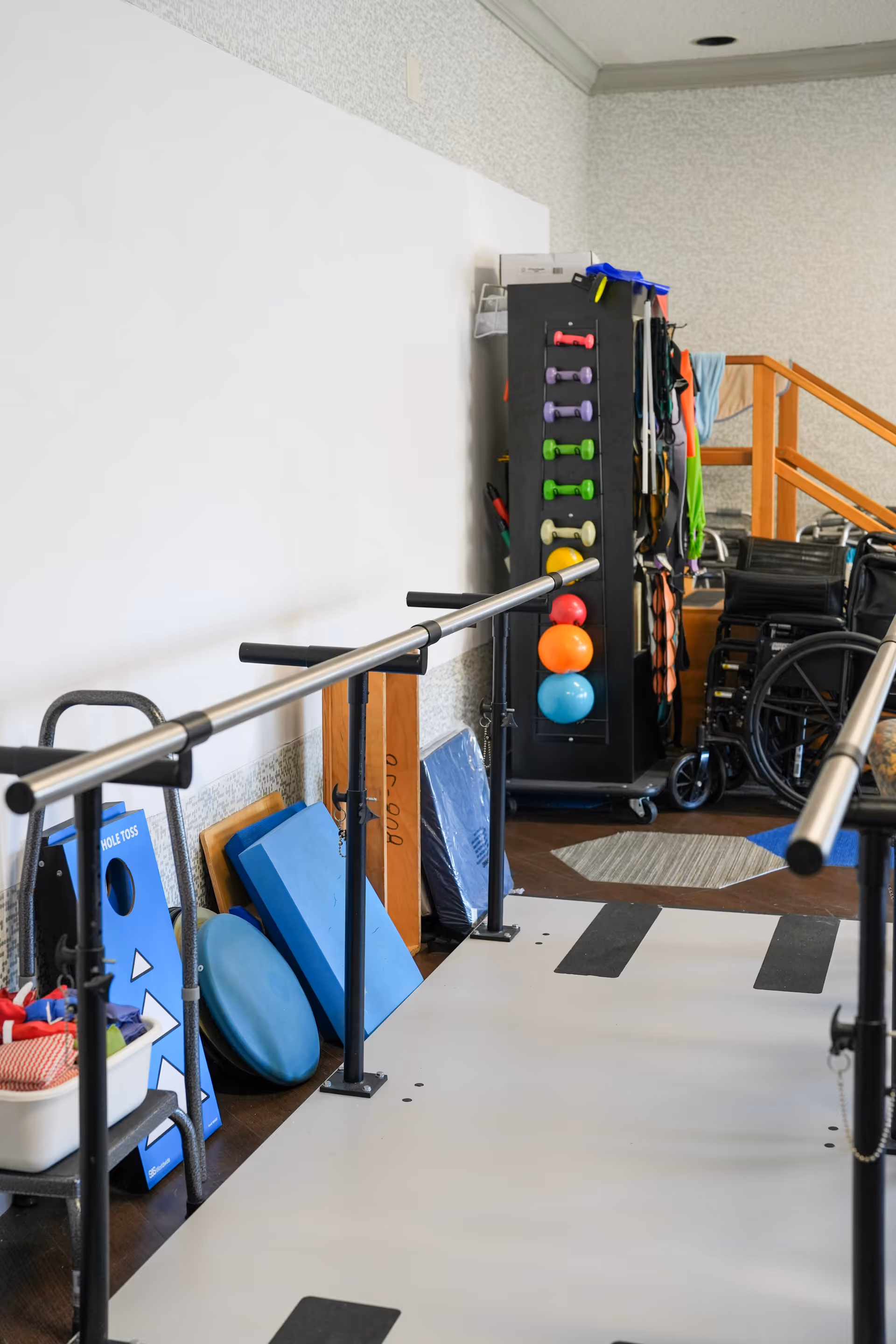 Physical therapy/exercise room with parallel bars, hand weights, exercise balls and wheelchairs.