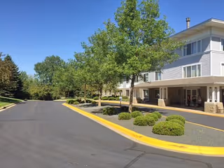 Driveway and landscaped entrance of a two-story residential building with a covered entry and trees.