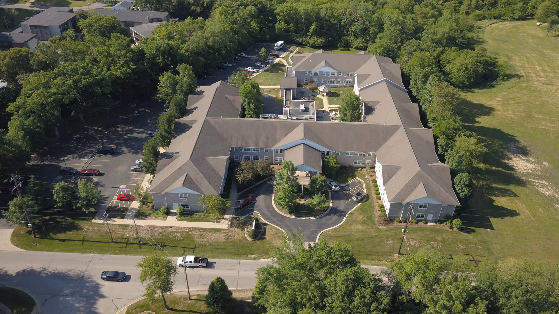 Aerial view of a senior living facility named Eagle Ridge of Decatur, showing a large, U-shaped building surrounded by trees and greenery with a parking lot on the left side and a road in the foreground.