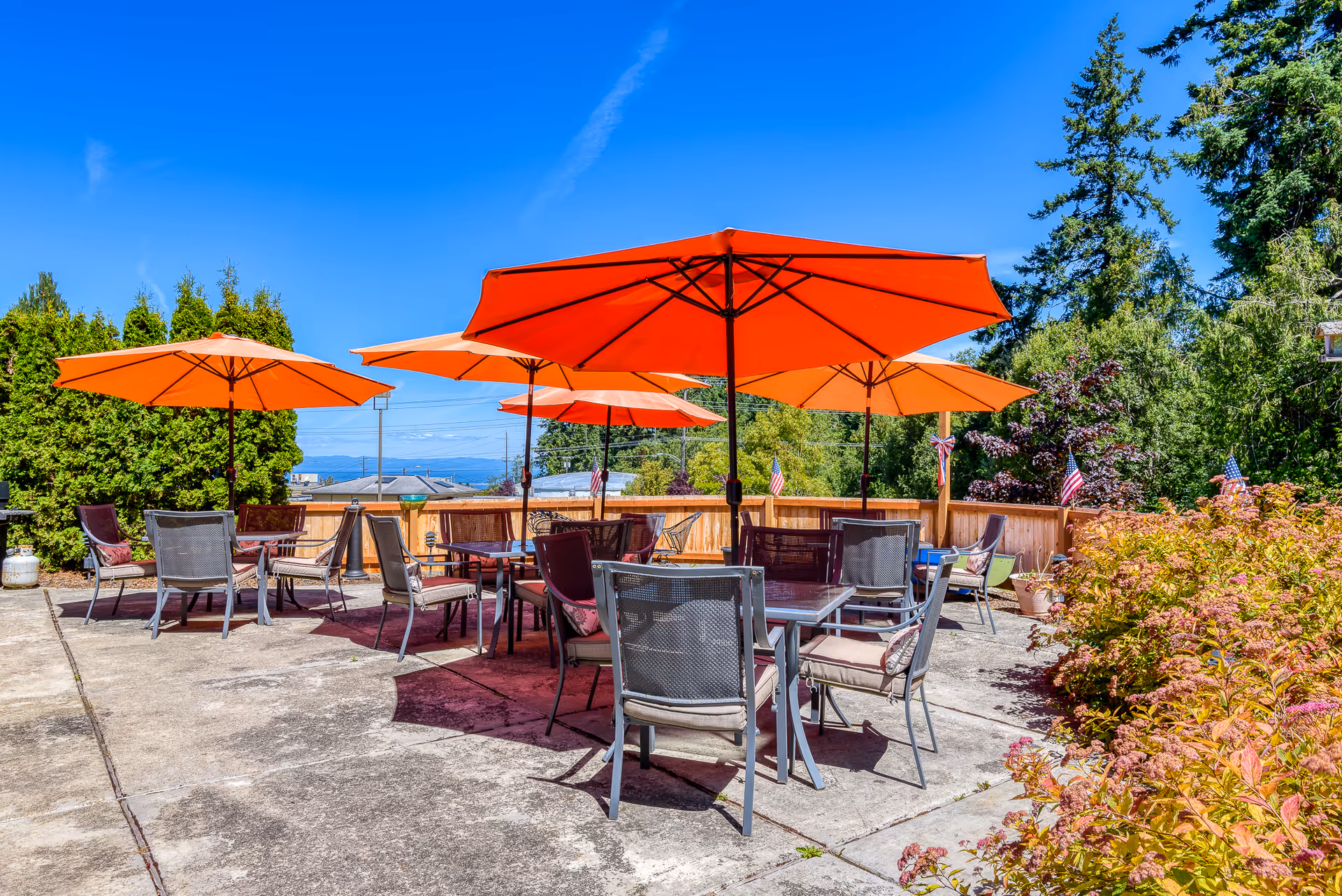 Outdoor patio with multiple tables, chairs, and bright orange umbrellas on a sunny day.