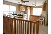 Open kitchen with a central island, white appliances, wood cabinets, large windows, and a wooden railing in the foreground.