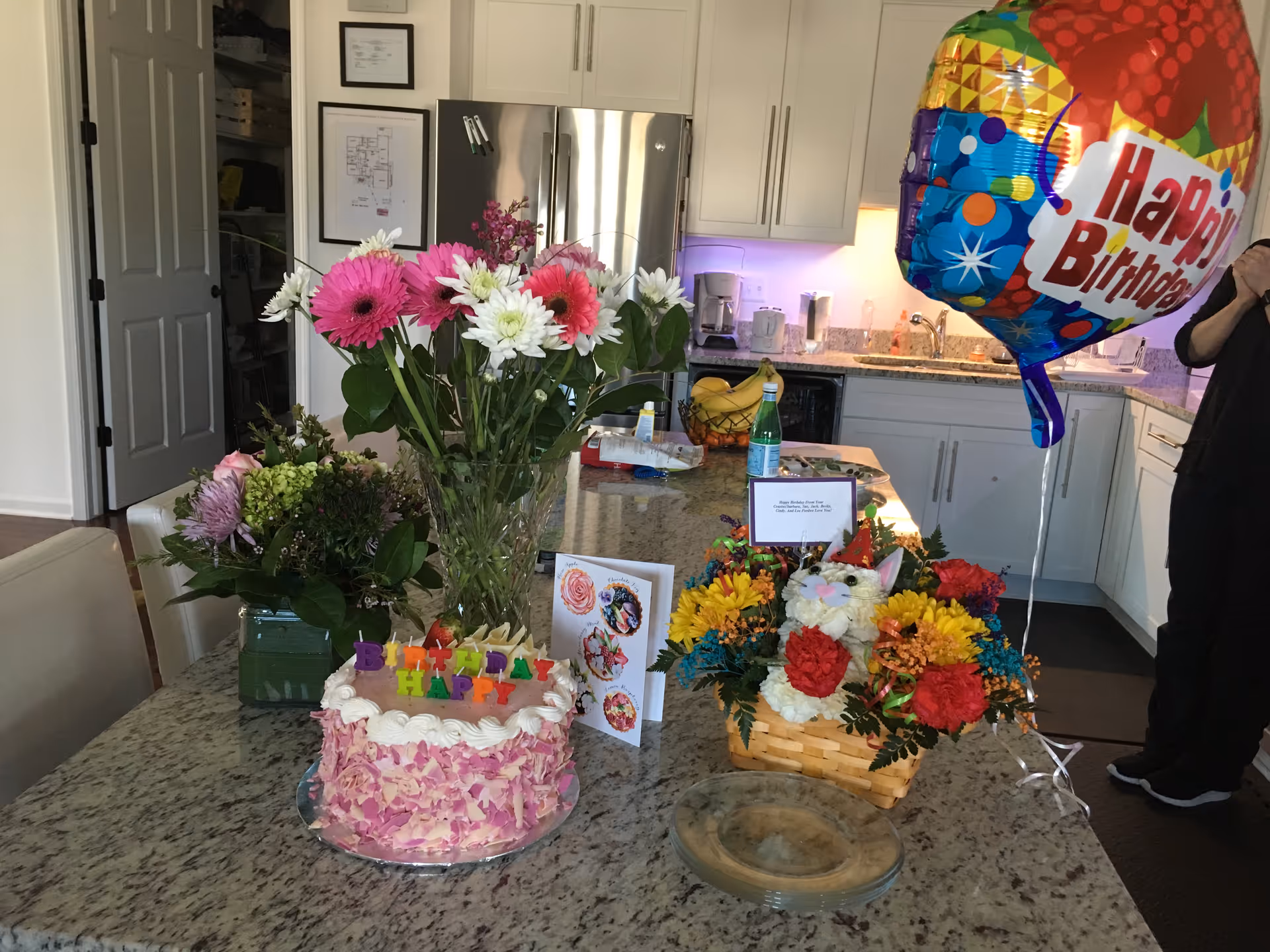 Birthday setup on a kitchen island with flowers, cake, and balloons.