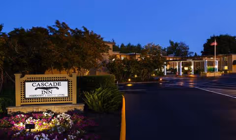 Exterior view of Cascade Inn Assisted Living Community with sign, parking lot, and entrance at dusk.