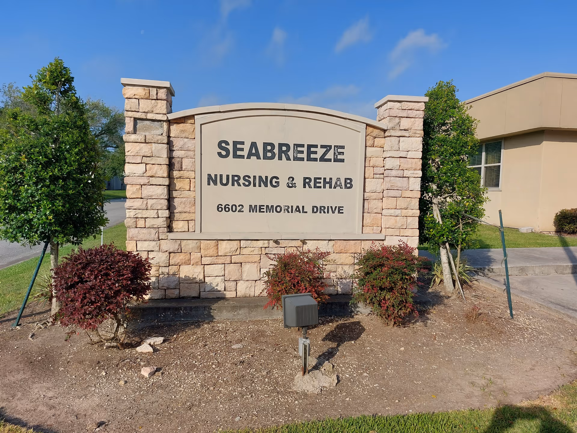 Stone monument sign reading "Seabreeze Nursing & Rehab, 6602 Memorial Drive" in front of a beige building with shrubs and a blue sky.