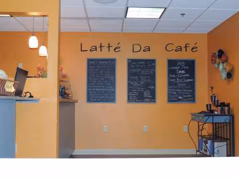Indoor cafe area labeled Latté Da Café with chalkboard menus and beverage cart