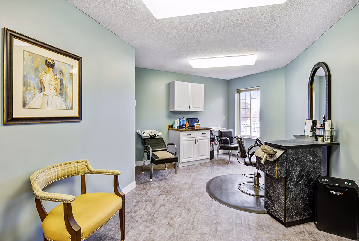 Interior salon room with styling chair, shampoo sink, cabinets and seating in a senior living facility.