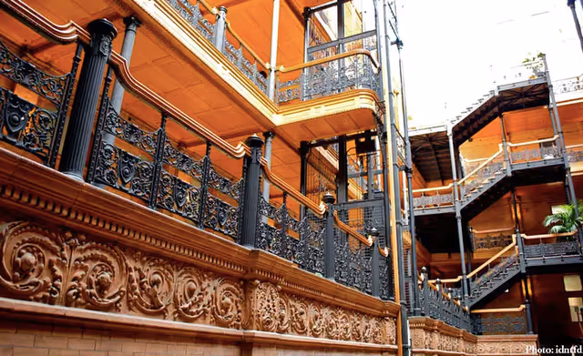 Interior view of a multi-level building featuring ornate black wrought iron railings and decorative brown stonework along the walls, with wooden ceilings and a staircase leading to upper floors.