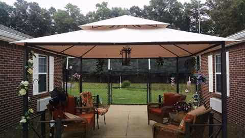 A brick courtyard with outdoor seating under a large umbrella and a green lawn beyond.