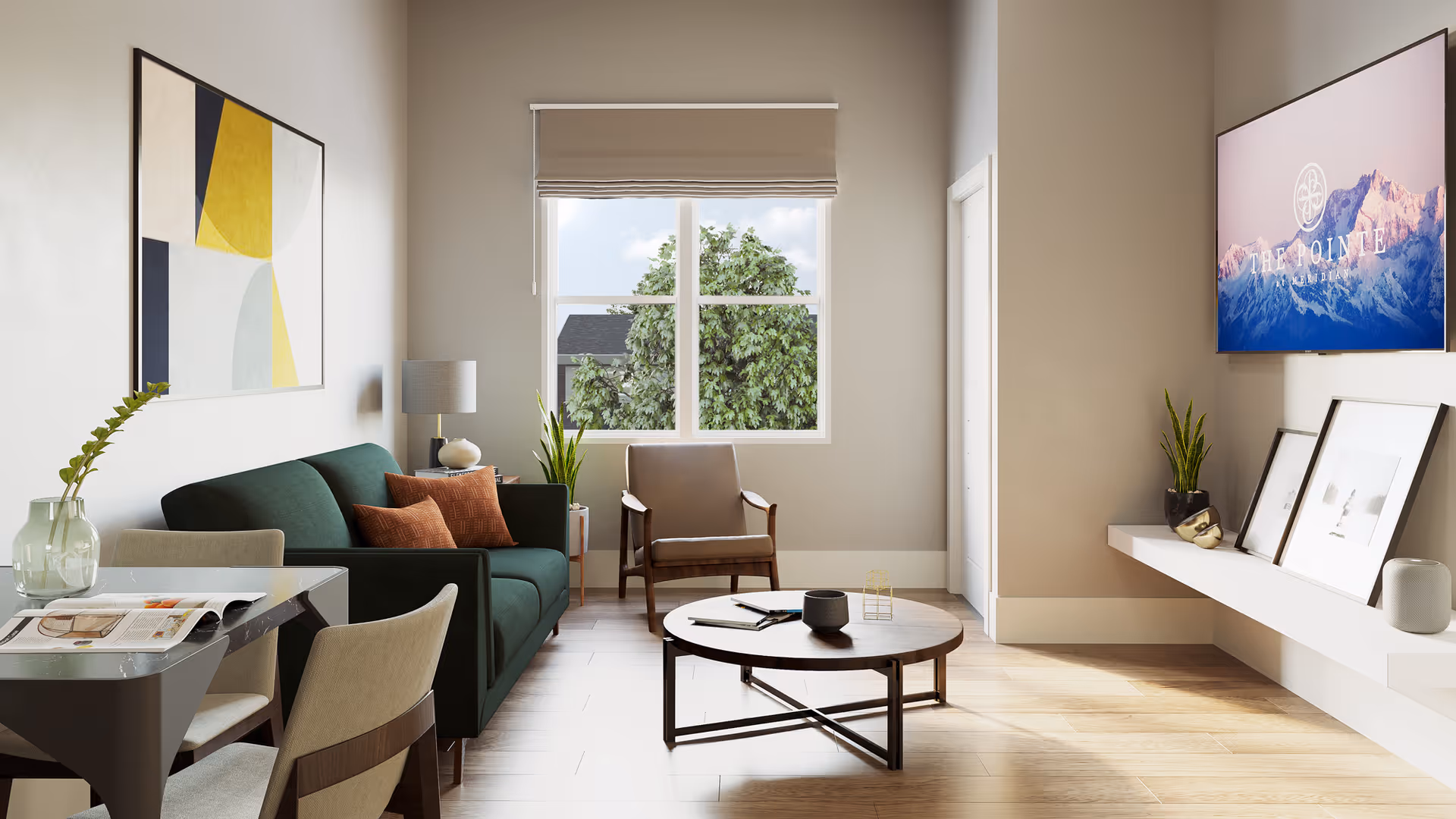 A modern living room with a green sofa adorned with brown cushions, a wooden armchair, and a round coffee table. There is a large window with a beige blind letting in natural light, a piece of abstract art on the wall, and a floating shelf with framed pictures and plants. A TV mounted on the wall displays an image of mountains with the text 'The Pointe'.