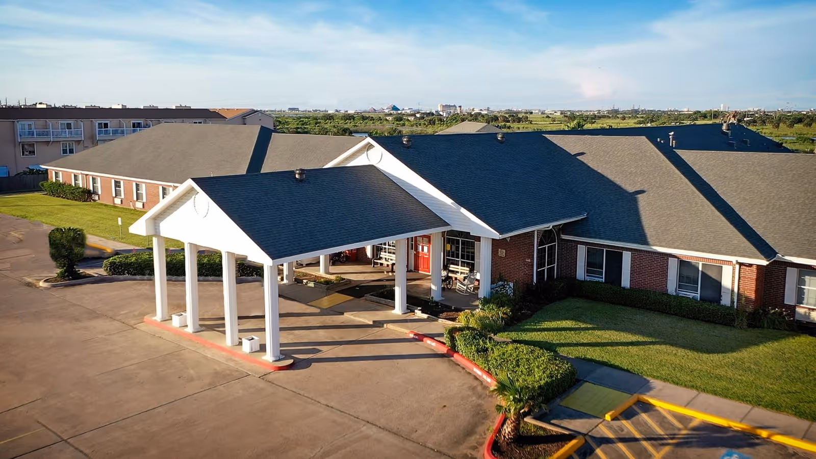 Exterior view of Cascades at Galveston facility showing a single-story brick building with a covered entrance supported by white columns, surrounded by well-maintained landscaping and a paved driveway.
