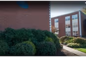 Exterior view of a brick senior living facility with a walkway and trimmed bushes.