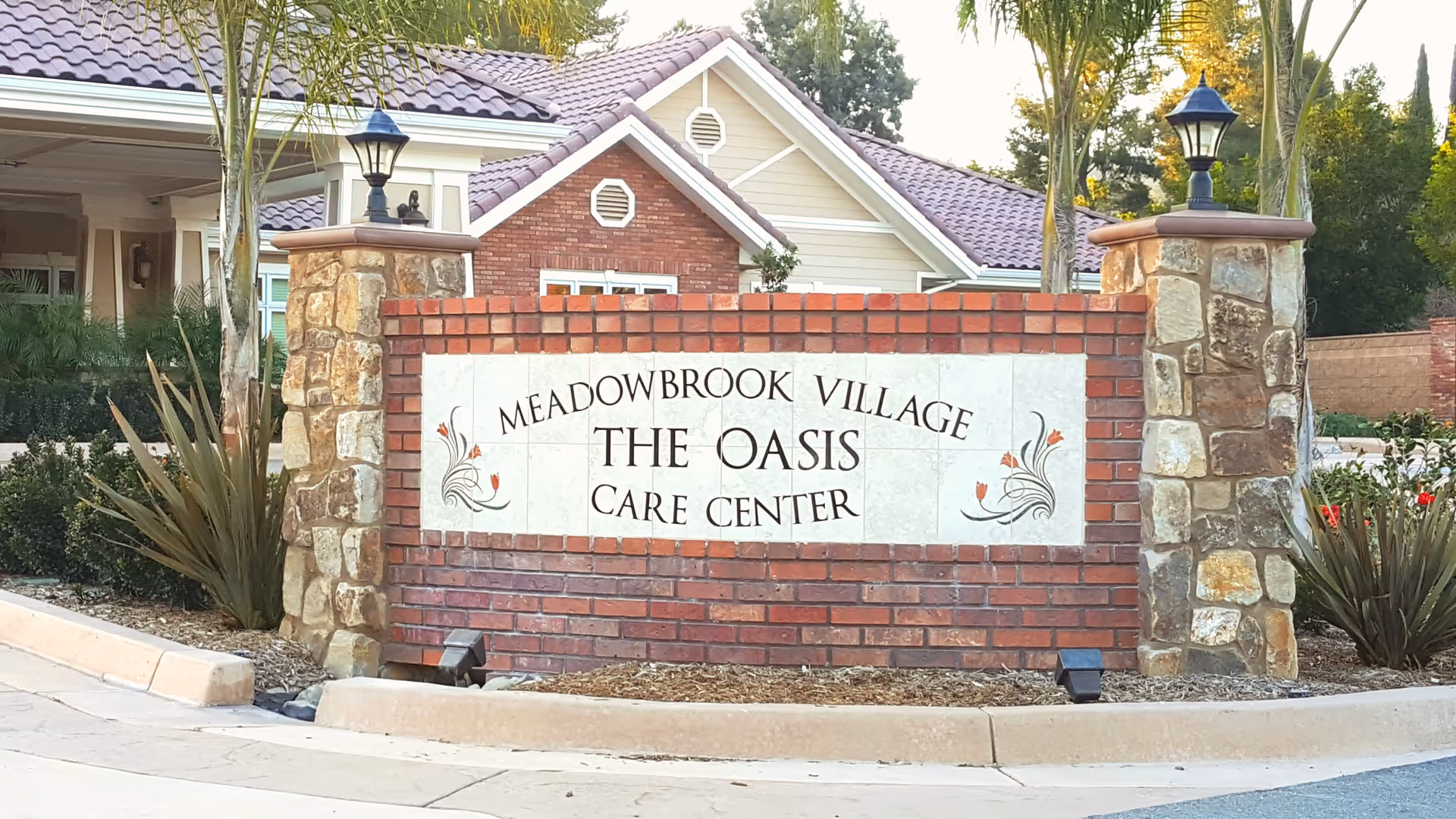Brick and stone entrance sign reading 'Meadowbrook Village The Oasis Care Center' in front of a residential-style building.