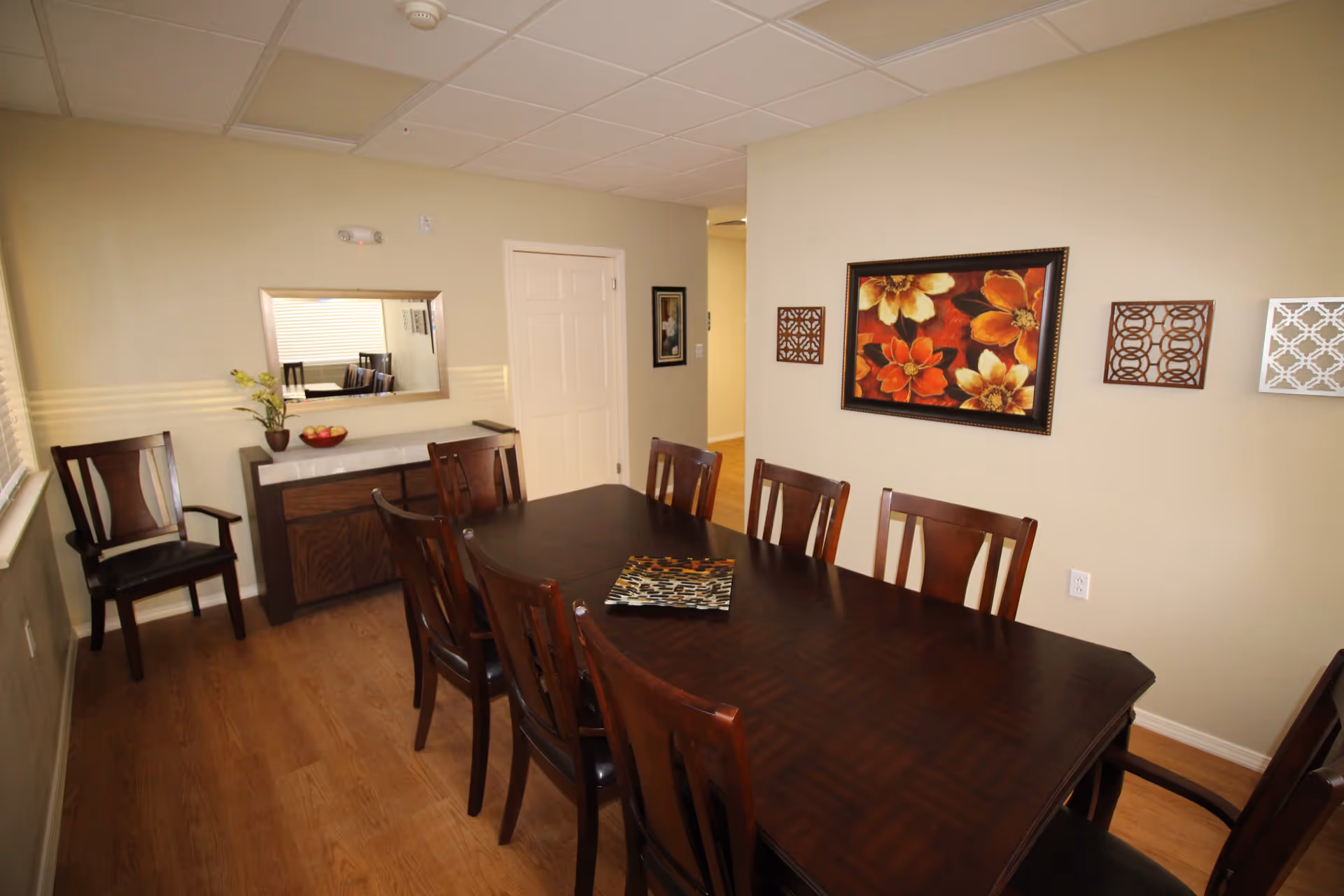 Dining room with a long dark wooden table and chairs, a sideboard with mirror, and floral wall art.
