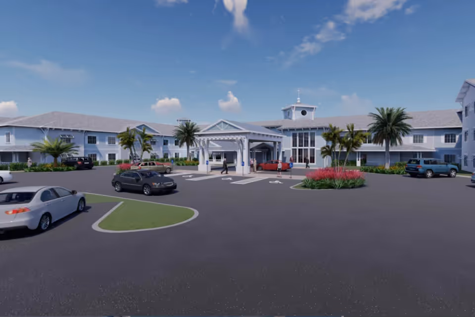 Exterior view of The Meridian at Punta Gorda Isles senior living facility showing a large two-story building with a covered entrance, palm trees, landscaped greenery, several parked cars, and a clear blue sky.