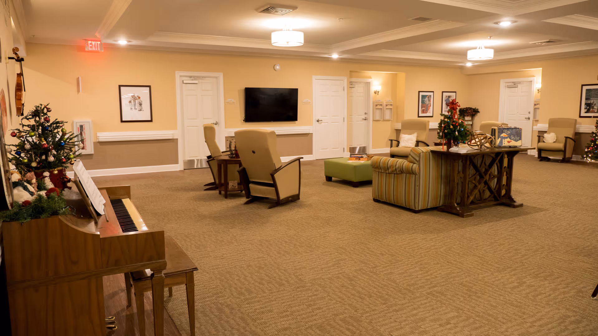 Spacious senior living common room with seating, a piano, a TV, and holiday decorations.