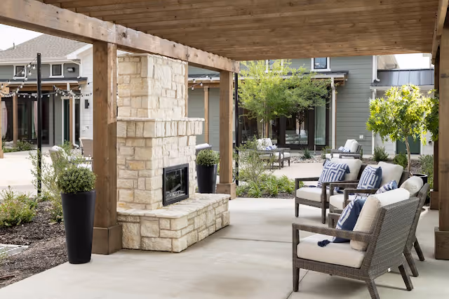 Covered outdoor patio with a stone fireplace, cushioned wicker chairs, and a landscaped courtyard.