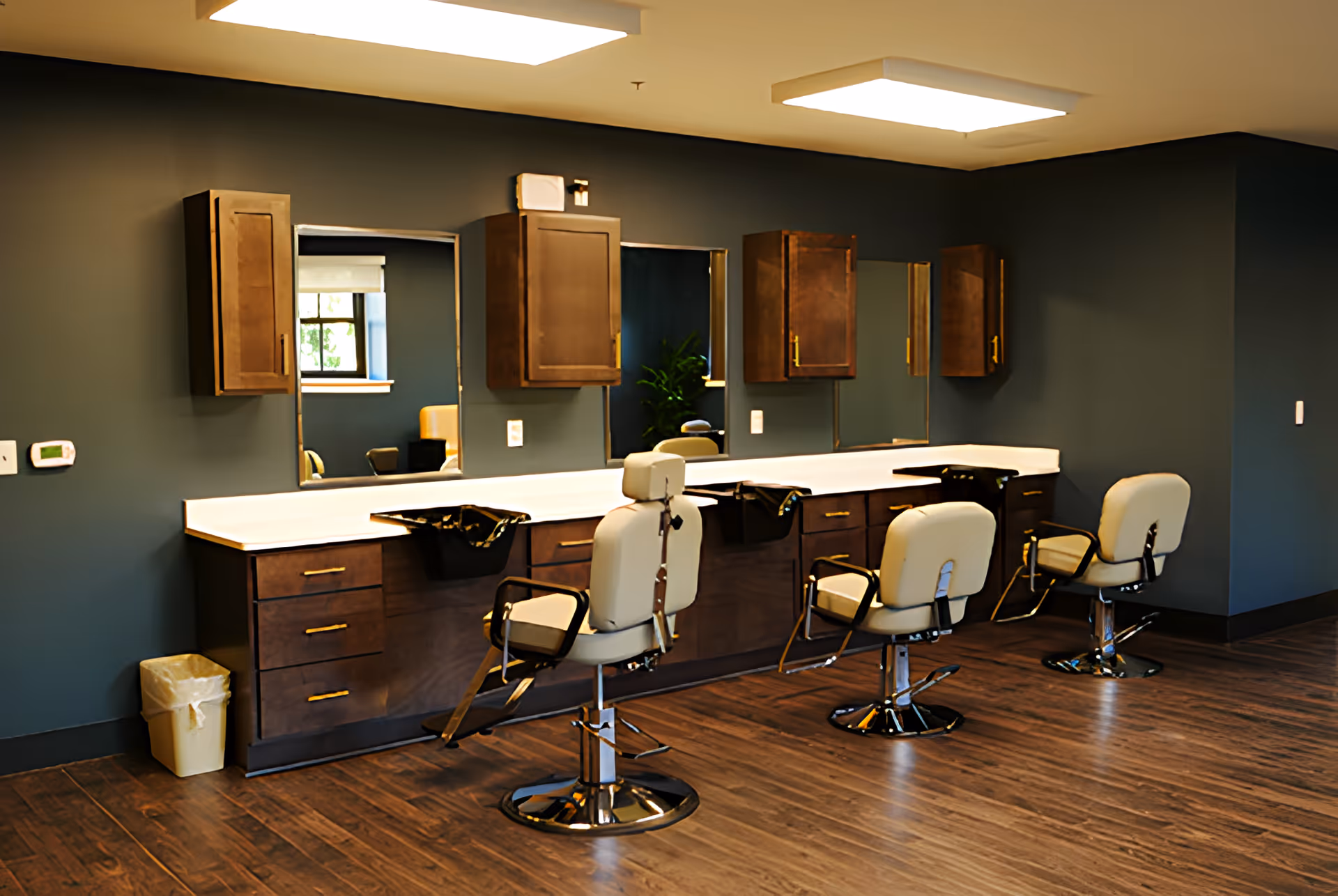 A salon-style room with three styling chairs in front of mirrors and dark wood cabinetry along a long counter.