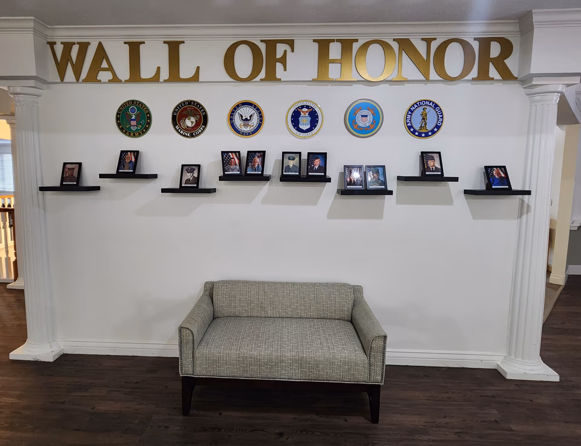 A bench in front of a 'WALL OF HONOR' display with military emblems and framed photos on small wall-mounted shelves.