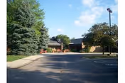 Exterior view of Willowbend Living Center showing a driveway leading to the entrance of a single-story brick building surrounded by trees and a parking area.