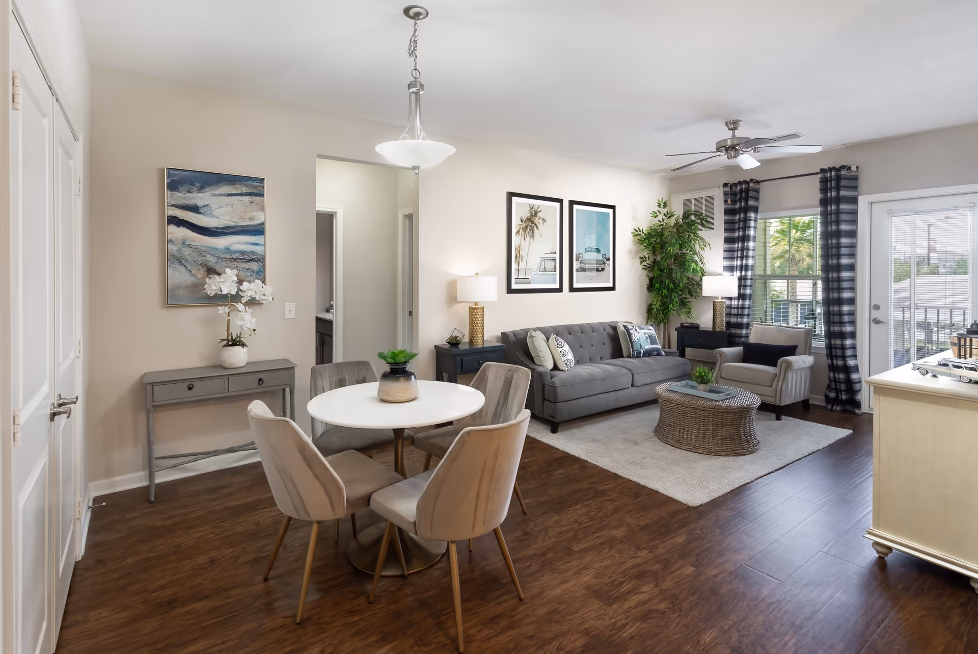 Open-plan living and dining area with a round table and chairs, gray sofa, armchair, coffee table, and sliding balcony door.