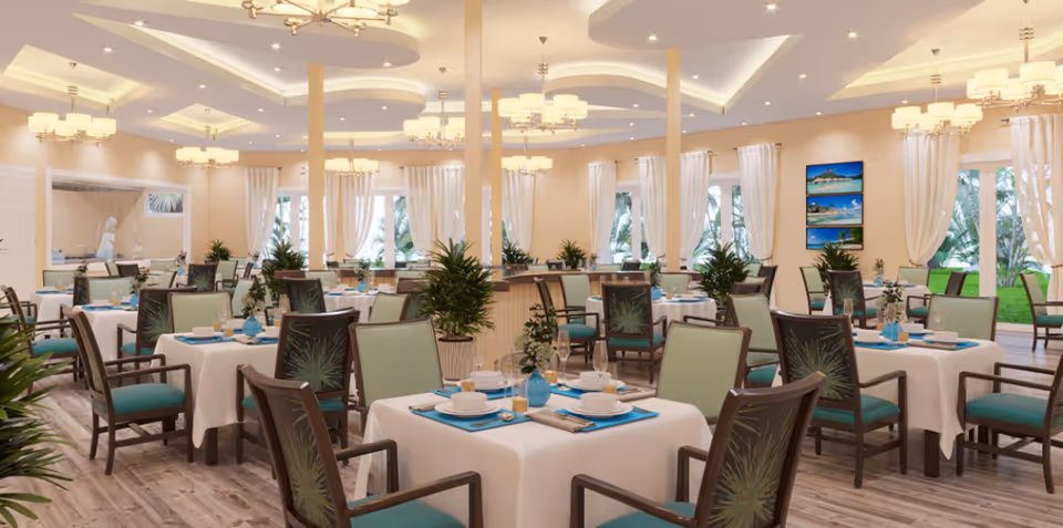 Well-lit dining room with multiple tables set with place settings, green upholstered chairs, and potted plants.