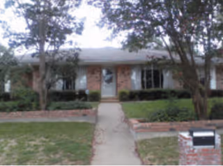A single-story brick facility exterior with a central walkway to the front entrance, surrounded by trees.