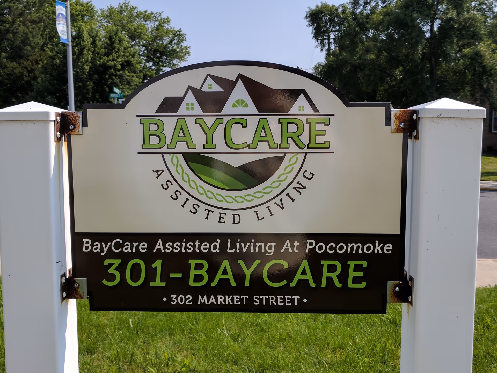 BayCare Assisted Living sign mounted on white posts at the facility entrance with green grass and trees in the background.