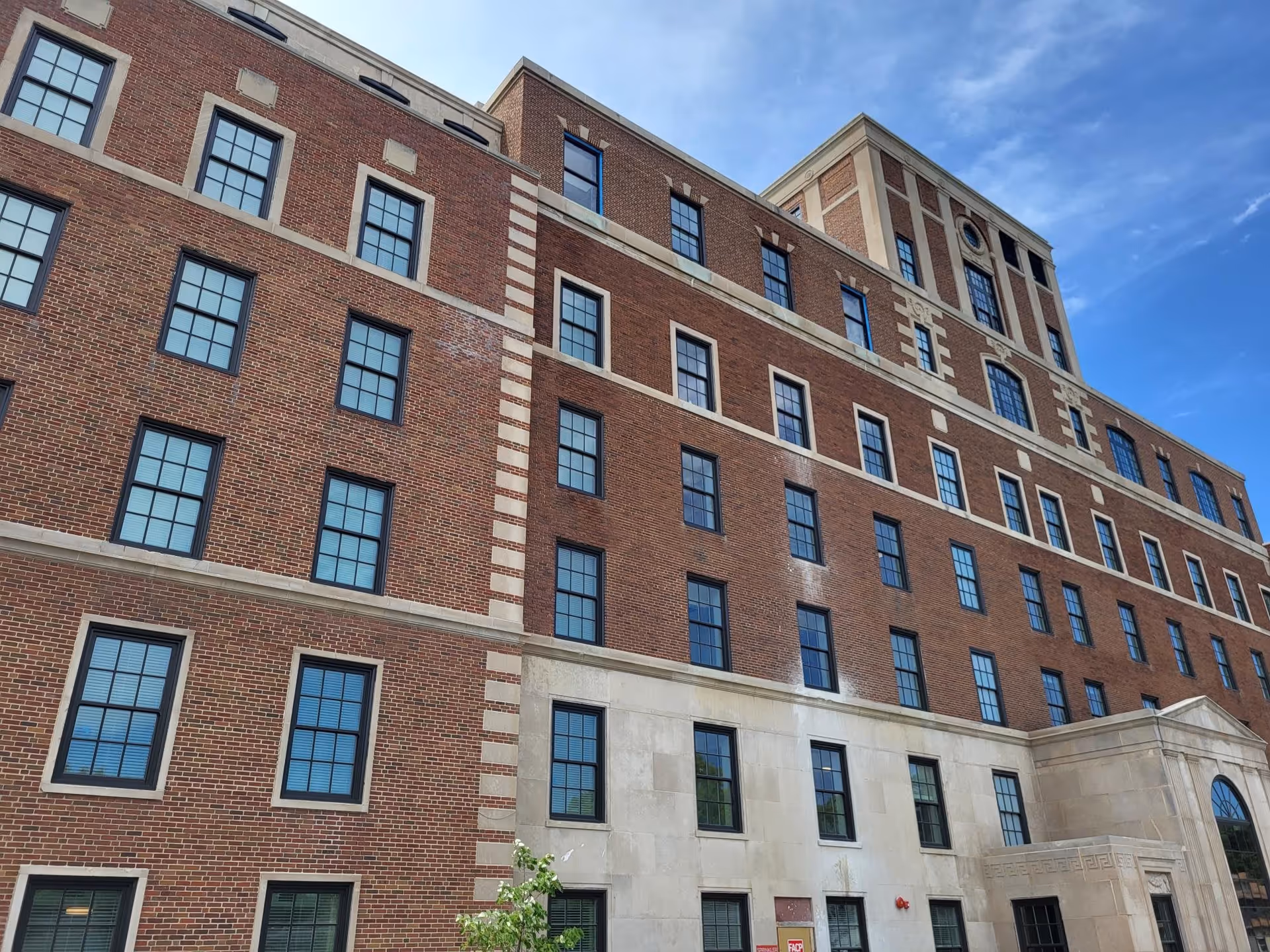 Exterior view of a multi-story brick building with numerous windows under a blue sky, showing the facade of Bardwell Residences.