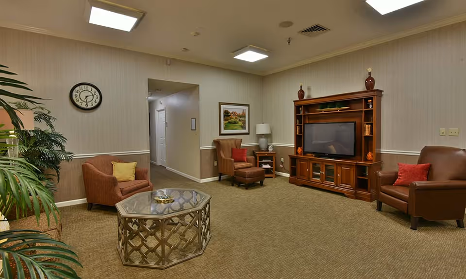 Comfortable common sitting room with upholstered chairs, a coffee table, TV cabinet, and plants.