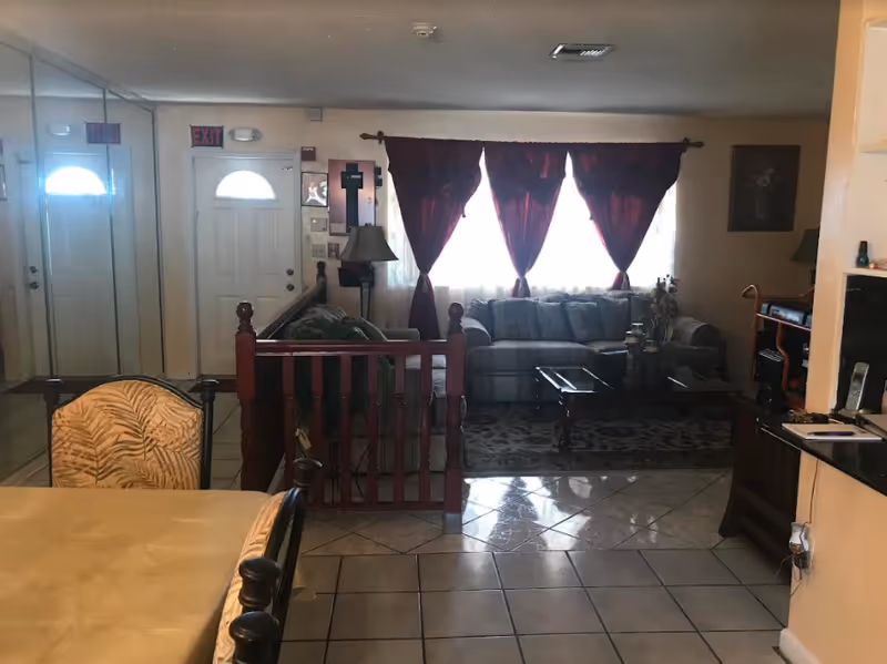 Indoor common area with a sofa, coffee table, curtains, dining table, and wooden railing.