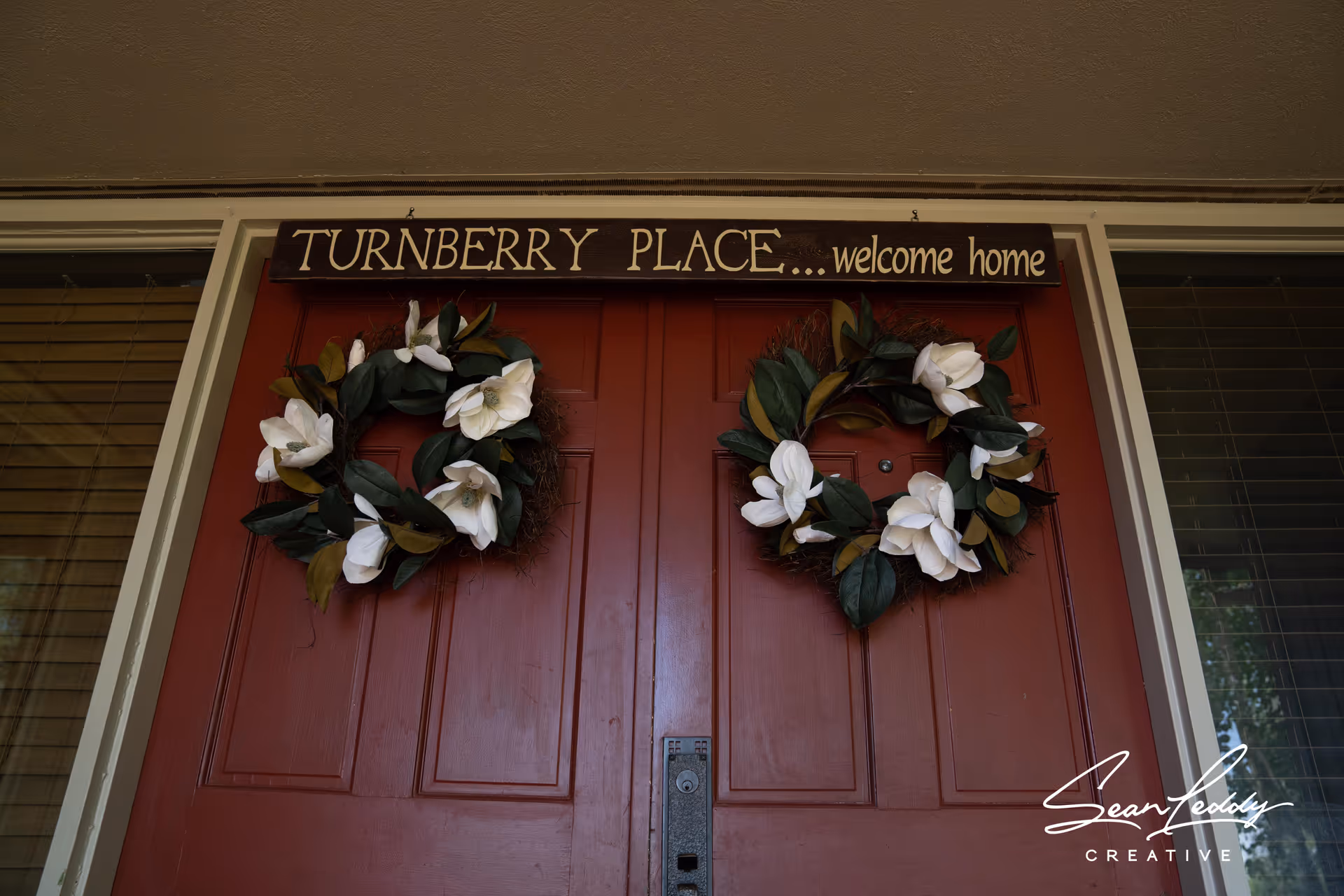 Red double front door decorated with two floral wreaths and a sign reading 'TURNBERRY PLACE... welcome home' above.