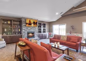 Spacious common living area with red sofas arranged around a stone fireplace, built-in shelving, coffee tables, and windows letting in natural light.