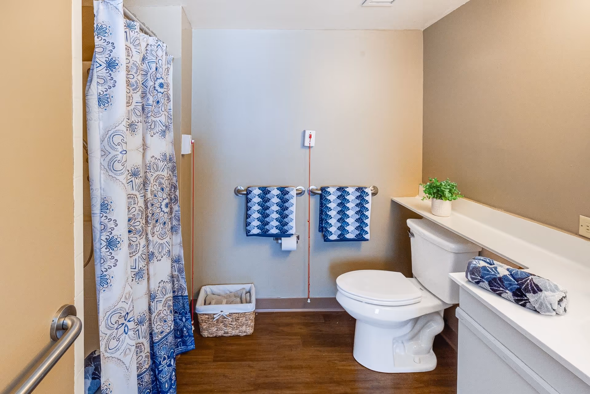 Accessible bathroom with a toilet, shower with a patterned curtain, grab bars, and blue patterned towels.