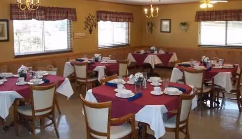 Dining room in a senior living facility with round tables and maroon and white tablecloths.