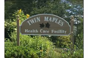 Twin Maples Health Care Facility sign amid greenery in a landscaped outdoor area.