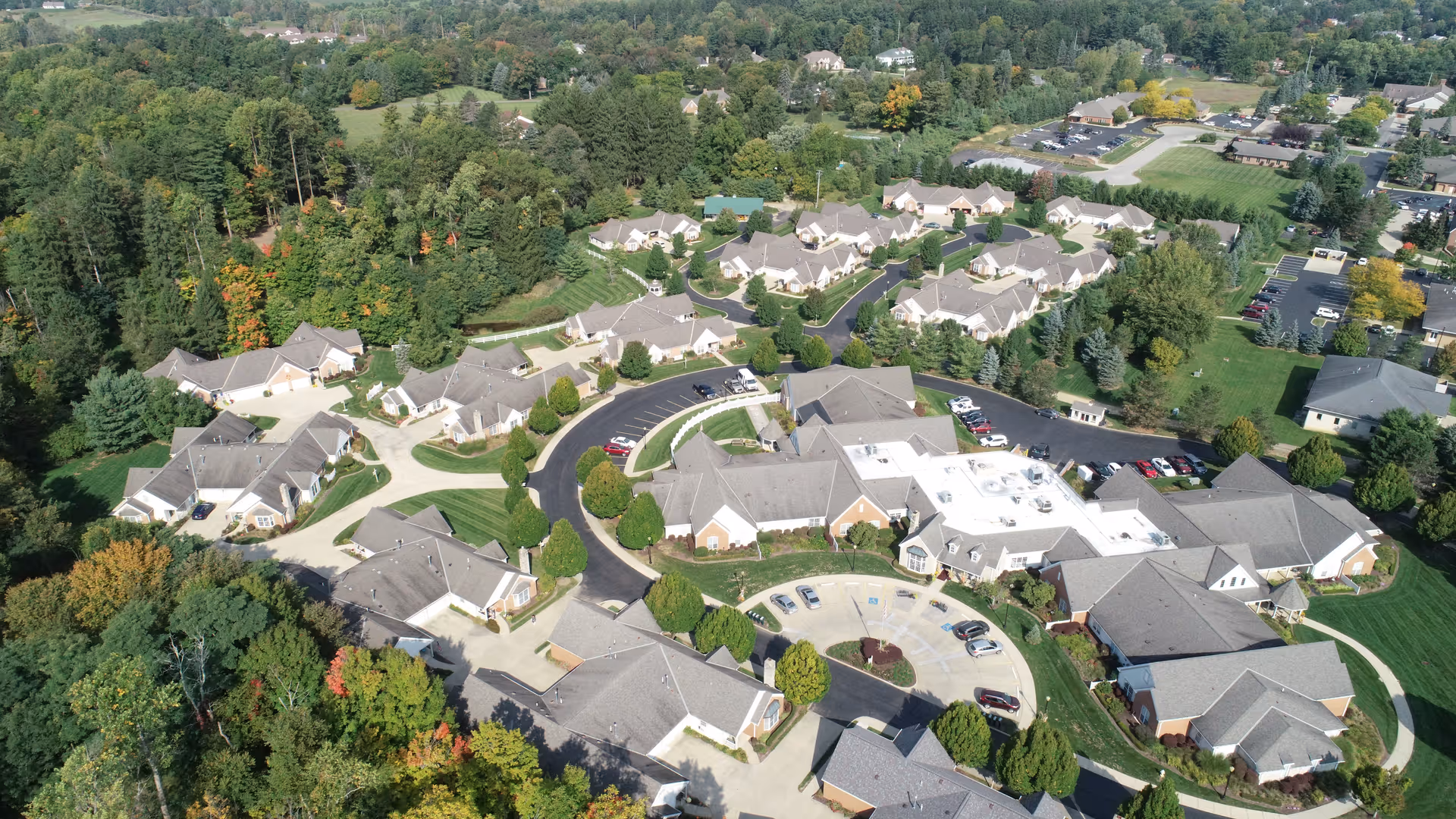 Aerial view of Wedgewood Estates senior living facility showing multiple single-story buildings with gray roofs arranged around curved roads and parking areas, surrounded by green lawns and trees.