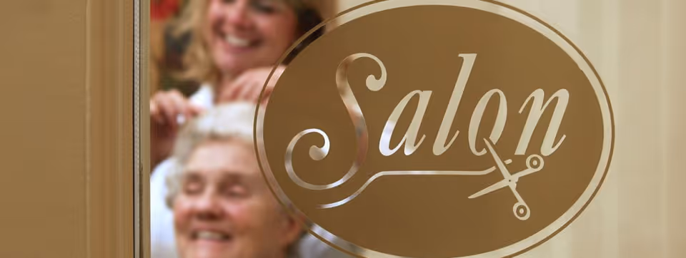 Frosted glass door with a gold "Salon" decal and blurred stylist and elderly client visible behind it.