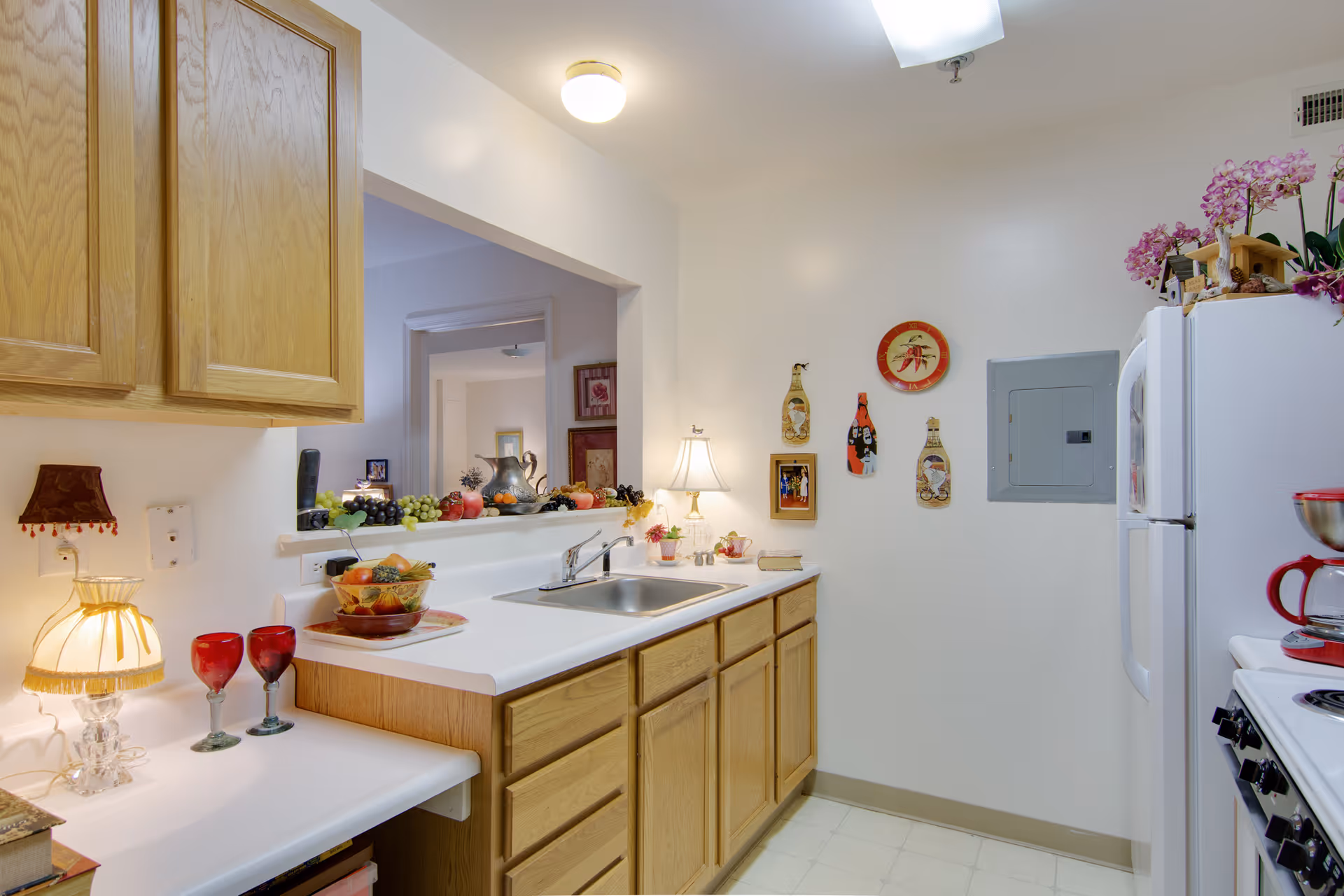 Bright kitchen with white countertops, oak cabinets, a sink under a pass-through, and decorative items and appliances.