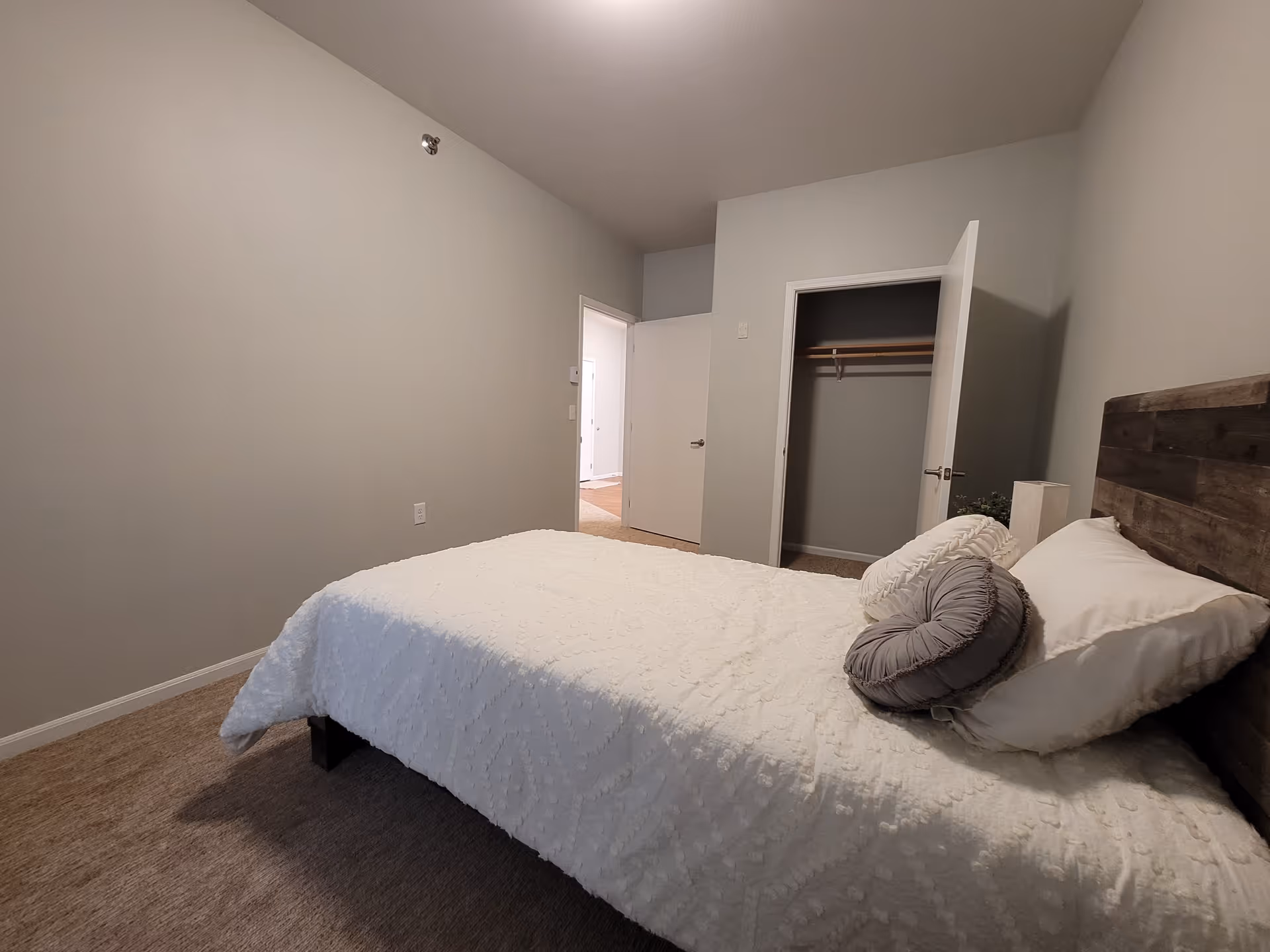 Bedroom with a white bedspread and pillows, a wooden headboard, an open closet, and a doorway to the hallway.