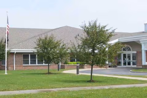 Front exterior of Father Baker Manor with flagpole, trees, and a curved entrance.