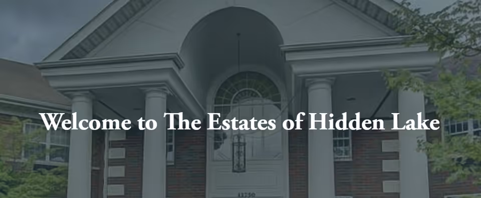 Front entrance of The Estates of Hidden Lake building featuring large white columns, a brick facade, and an arched window above the door with the text 'Welcome to The Estates of Hidden Lake' overlaid.