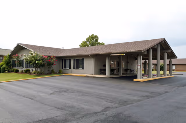 Single-story brick nursing and rehab building with a covered entrance canopy, parking area, and landscaped lawn.