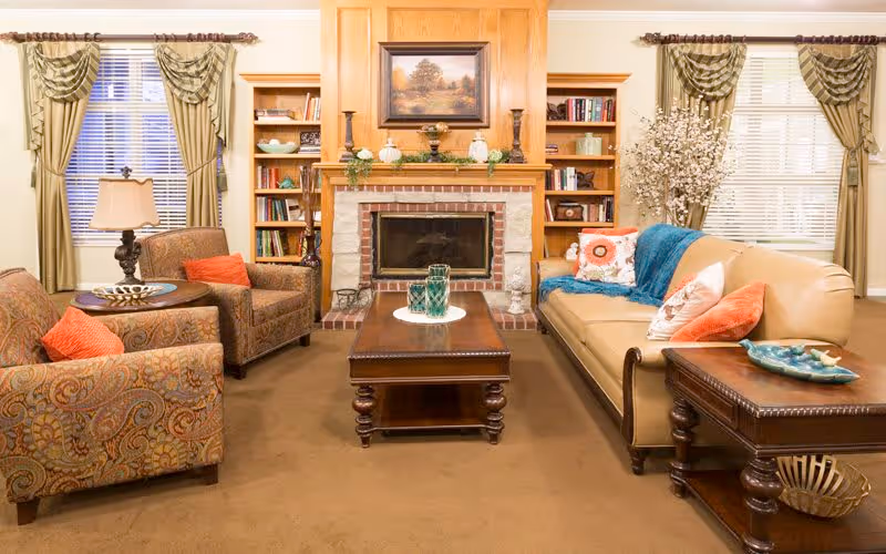 Cozy living room with a couch, patterned armchairs, a wooden coffee table and a fireplace flanked by built-in bookshelves.