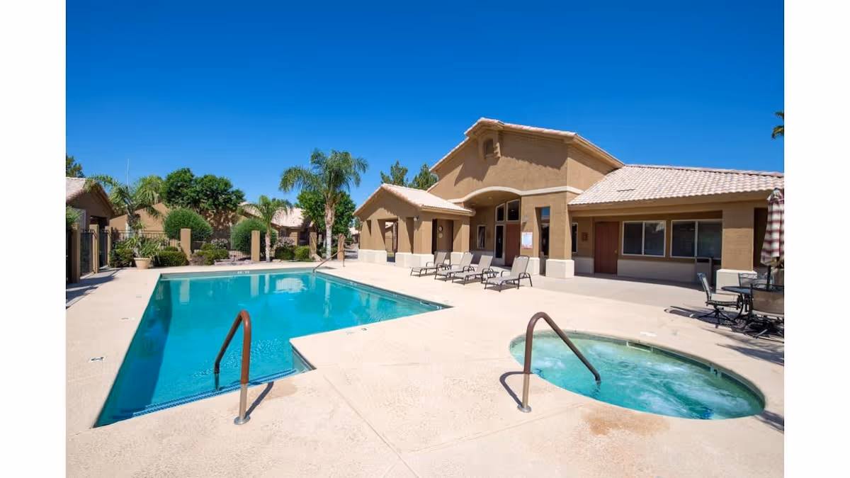 Outdoor swimming pool and hot tub area at Cypress Point facility with lounge chairs and a building with a tiled roof under a clear blue sky.
