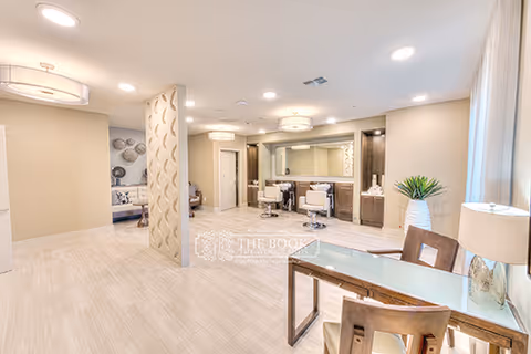 Bright modern senior living interior showing a reception/common area with seating, desks, and a decorative partition.