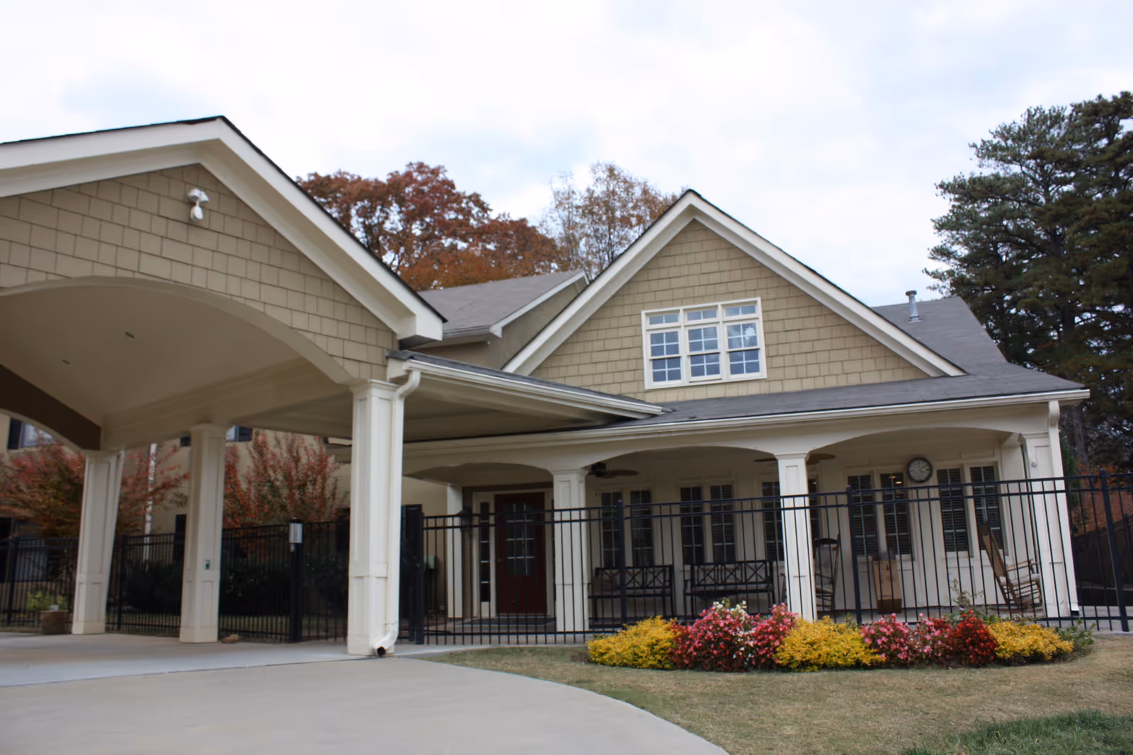Front exterior of a senior living building with a covered porte-cochère, columns, porch and landscaped flowerbed.