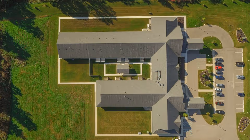 Aerial top-down view of a large senior living facility building with interior courtyards, surrounding lawns, and a parking lot.